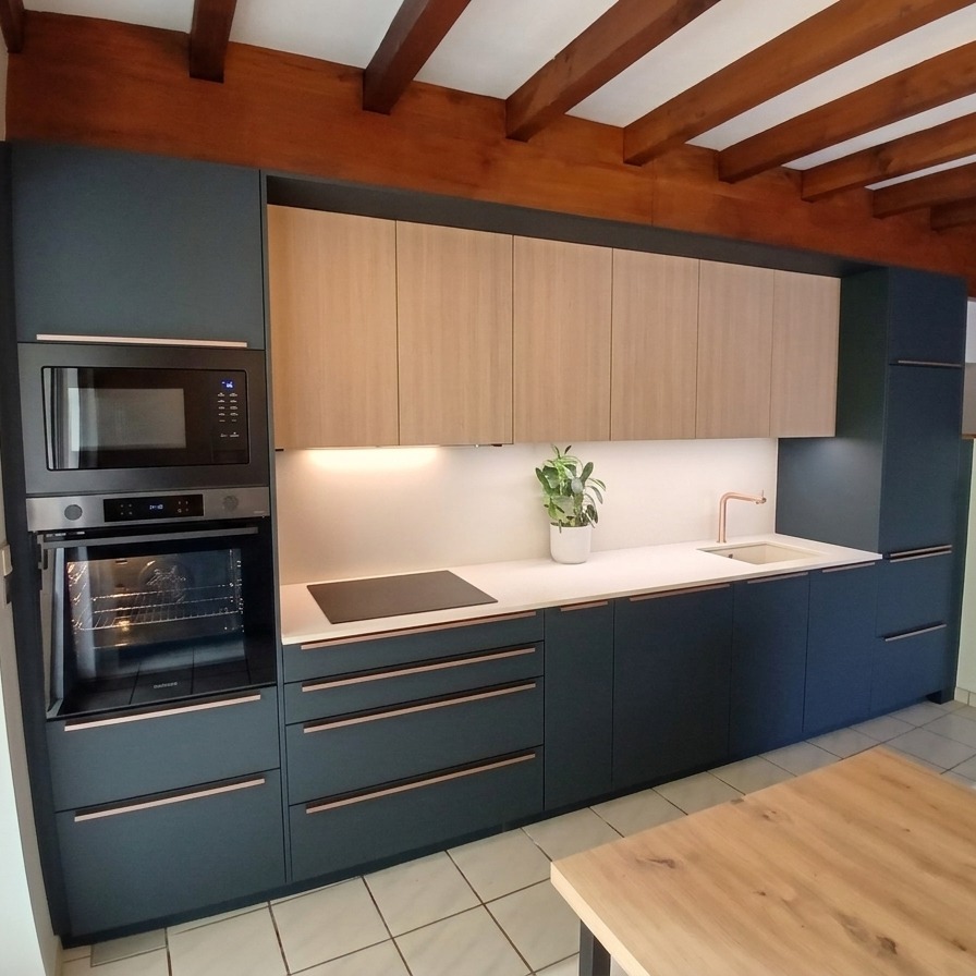 Résultat final d'une rénovation de cuisine moderne aux façades bleu mat sous charpente apparente, installée par NA Concept à Mauléon-Licharre.